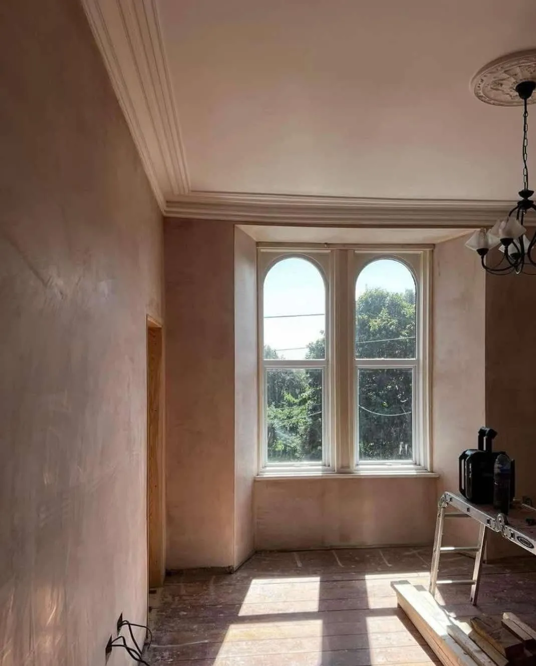 Freshly plastered walls and reveals around tall arched windows in a period room