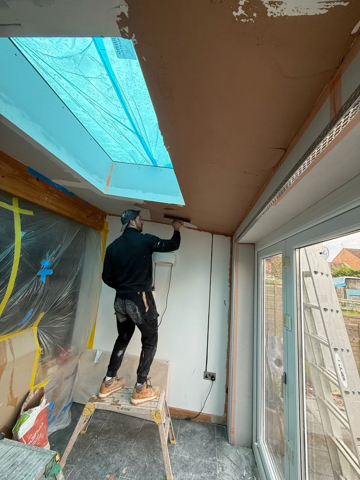 Plasterer using a trowel to finish a ceiling beside a rooflight in a protected room