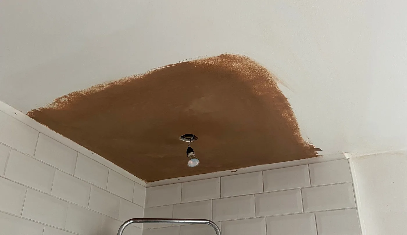 Local plaster patch in a white bathroom ceiling above tiled walls